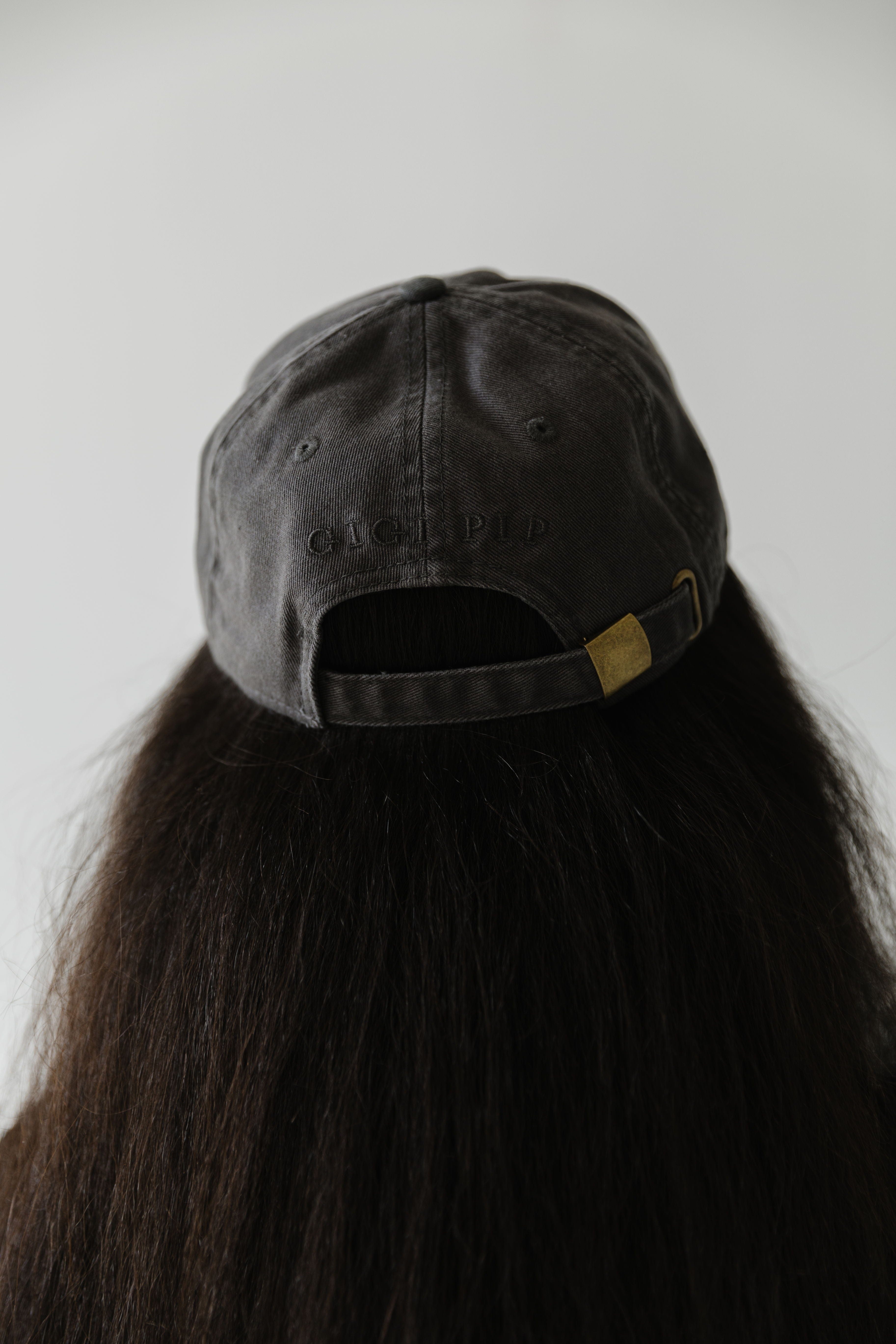 Woman with long hair wearing a dark grey ball cap facing behind against a plain background #color_dark grey-caramel