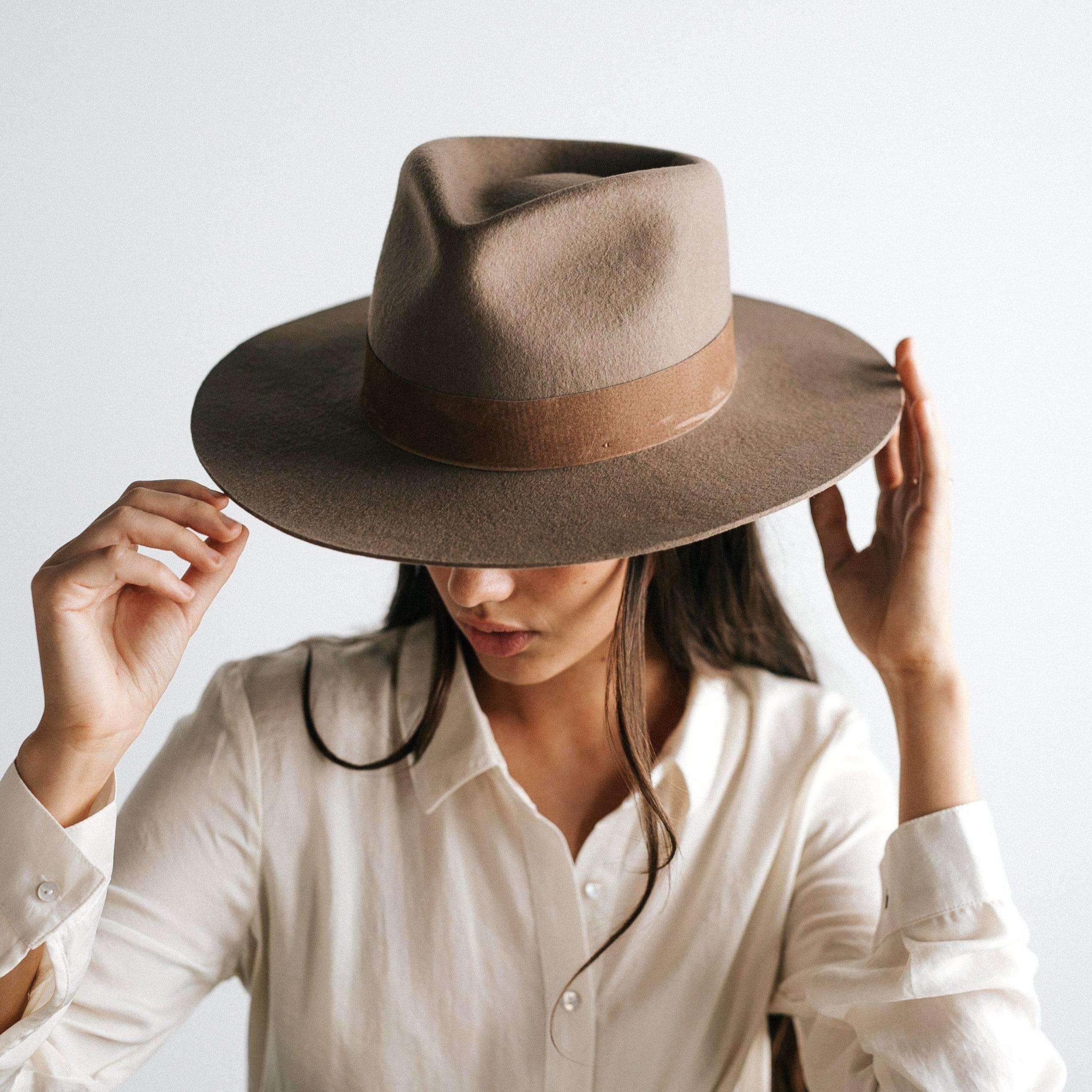 Woman wearing a brown fedora hat with a band and a white shirt, posing against a plain background #color_brown