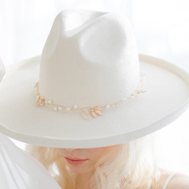 Close up image of a woman wearing a white hat with a delicate gold floral hat band against a plain background #color_gold