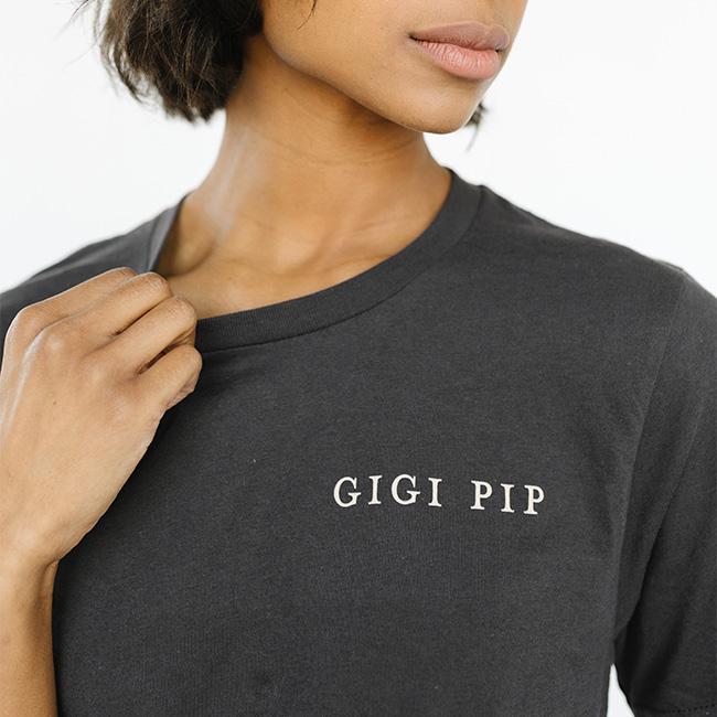 Woman wearing a graphite colored t-shirt with 'GIGI PIP' text against a white background #color_graphite