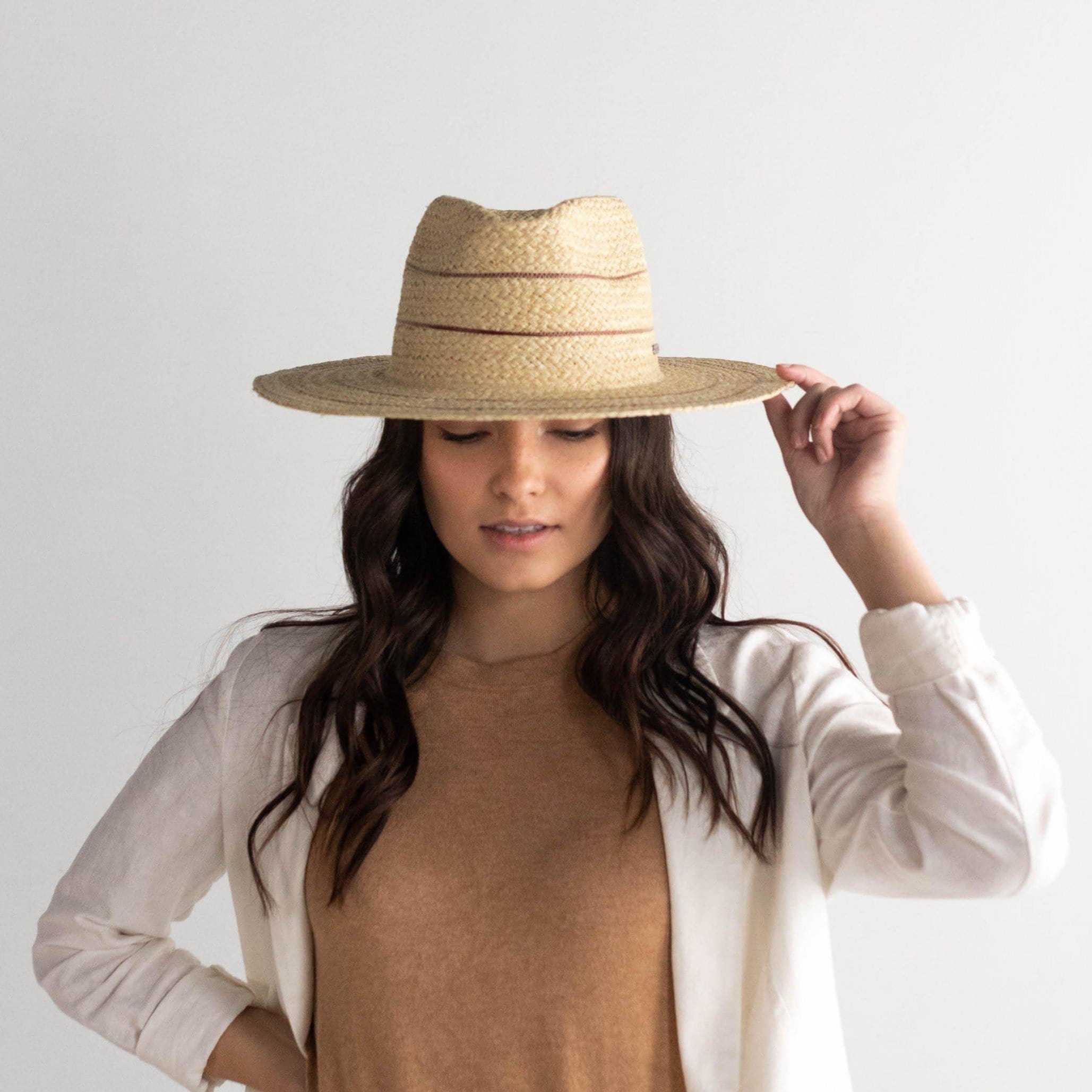 Woman wearing a natural colored straw fedora hat with stripes and a brown t-shirt with a cream jacket against a plain background #color_natural with stripes