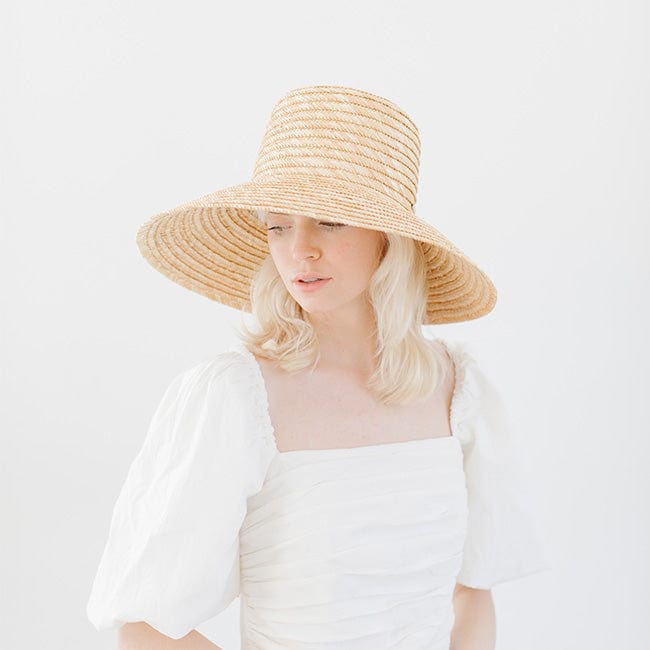 Woman wearing a natural colored straw boater hat and a white top, posing against a plain background #color_natural