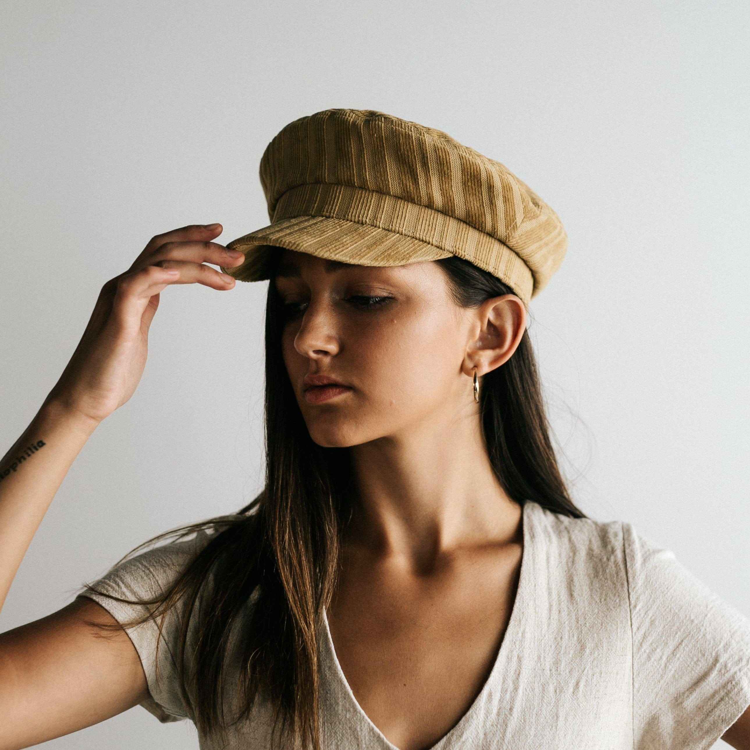 Woman wearing a mustard colored striped cap and a white t-shirt against a plain background  #color_mustard