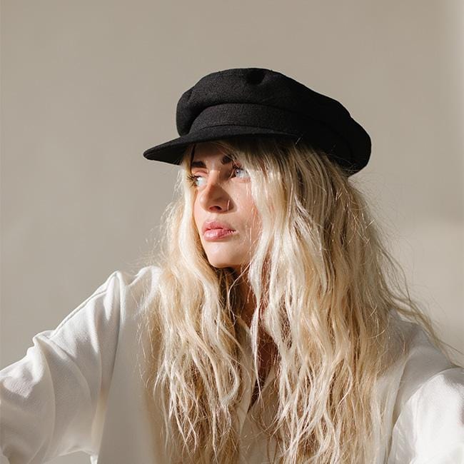 Woman wearing a black cap and a white shirt, posing against a plain background #color_black