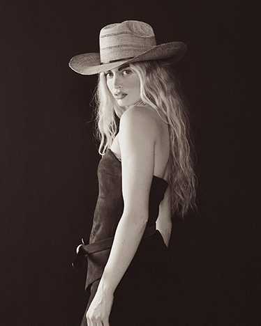 A black and white image with a woman wearing a straw hat against a black background 