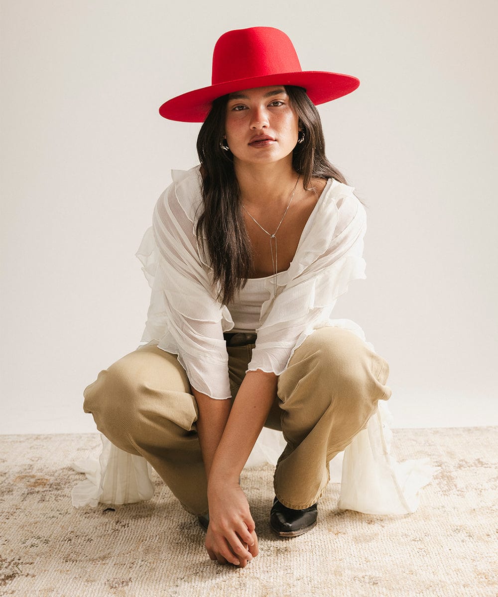 Woman wearing a red hat, white shirt, and beige pants on a plain background #color_cherry red