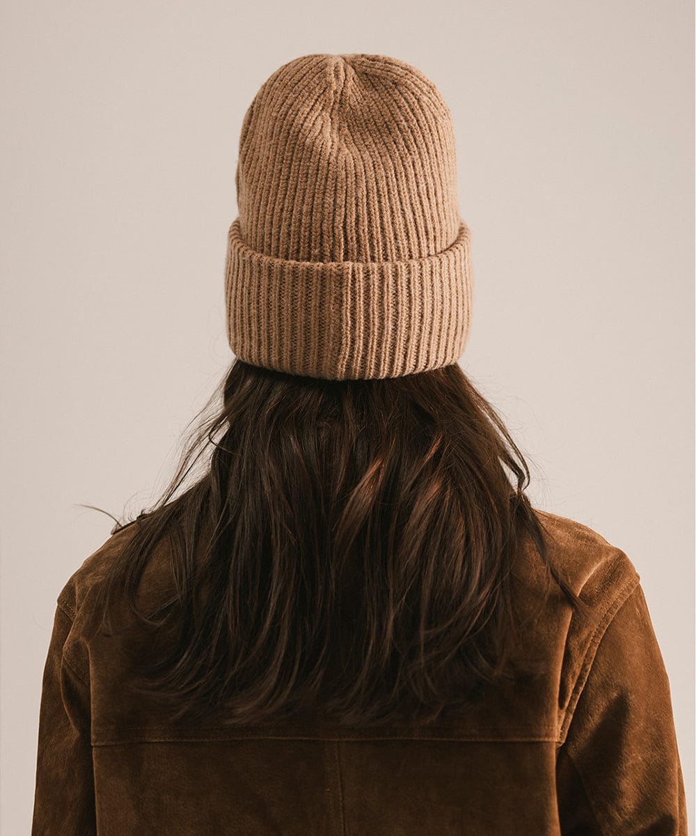 Person wearing a brown knit beanie and jacket, facing behind against a plain background #color_brown