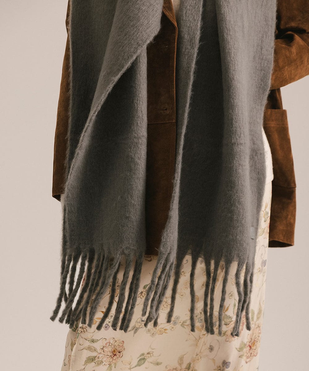 Gray scarf with fringes draped over a brown coat on a neutral background #color_grey
