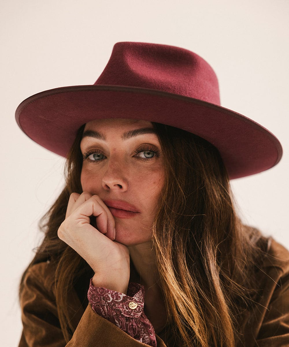 Woman wearing a maroon hat and brown coat with a neutral background #color_merlot