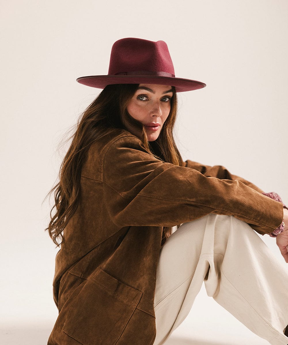Woman wearing a brown jacket and maroon hat against a plain background #color_merlot