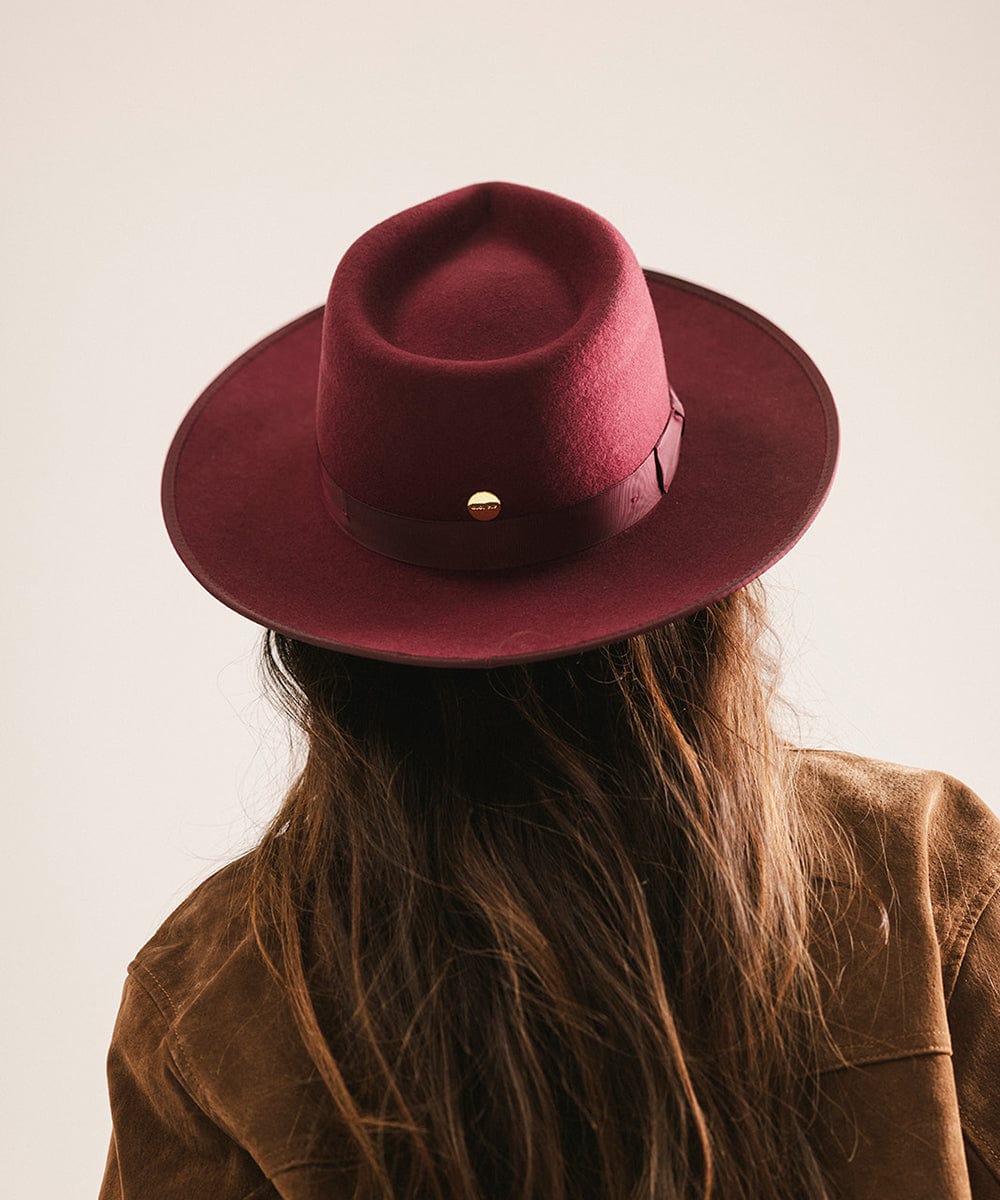 Person wearing a maroon fedora hat with a gold button on a plain background #color_merlot