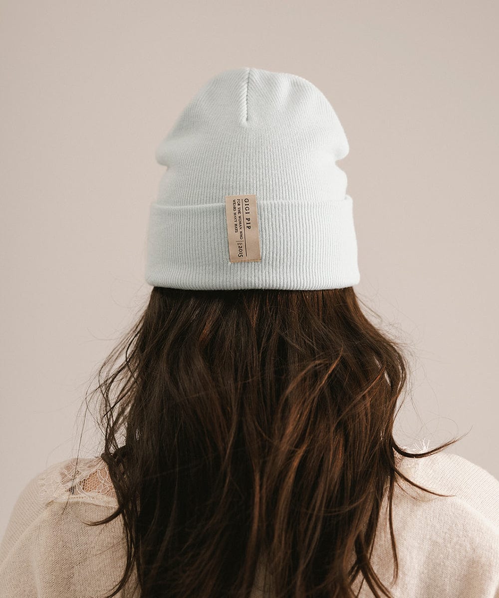 Light blue beanie with a label worn by a person against a beige background #color_sky blue