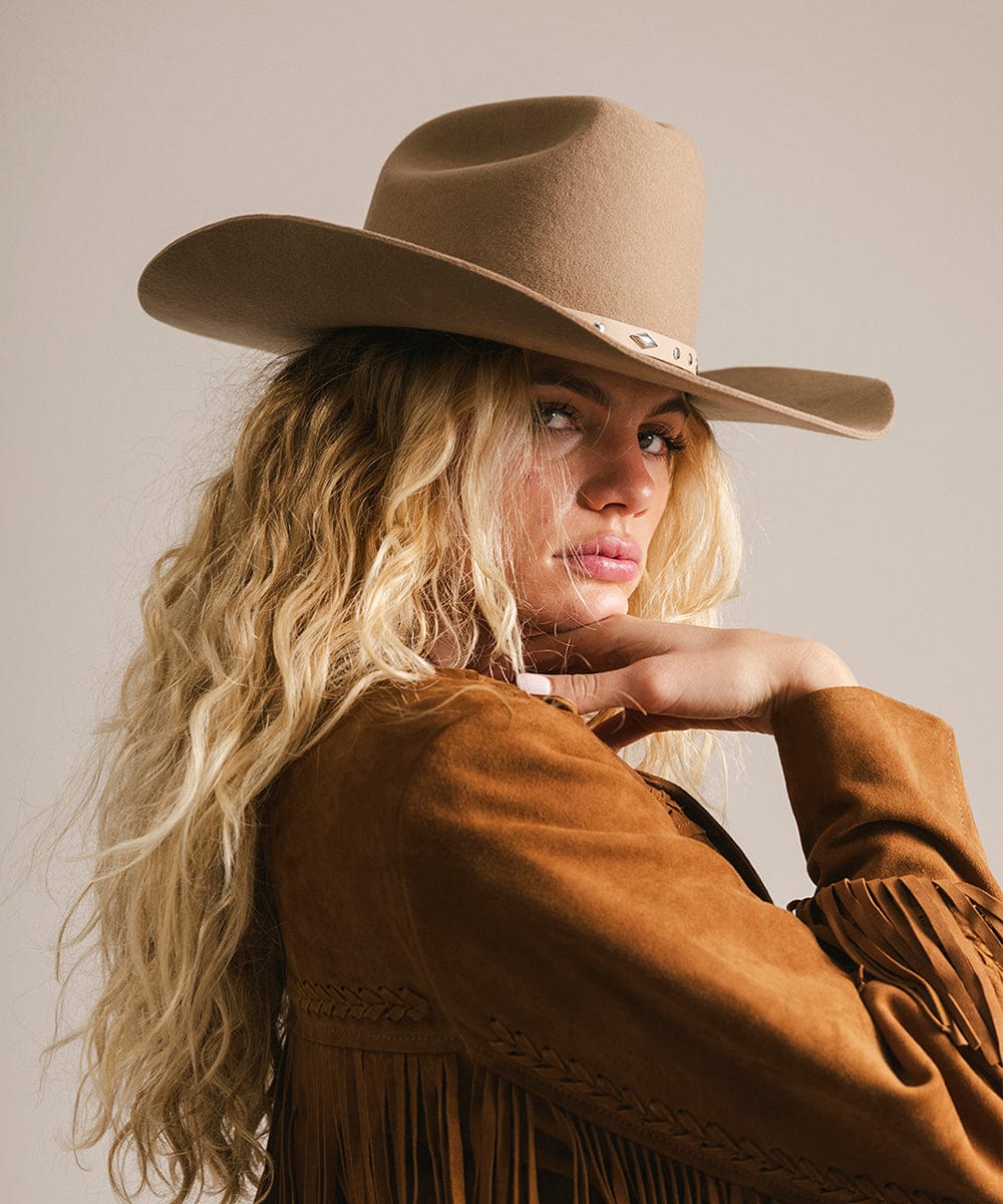 Woman wearing a brown cowboy hat and jacket against a neutral background #color_brown