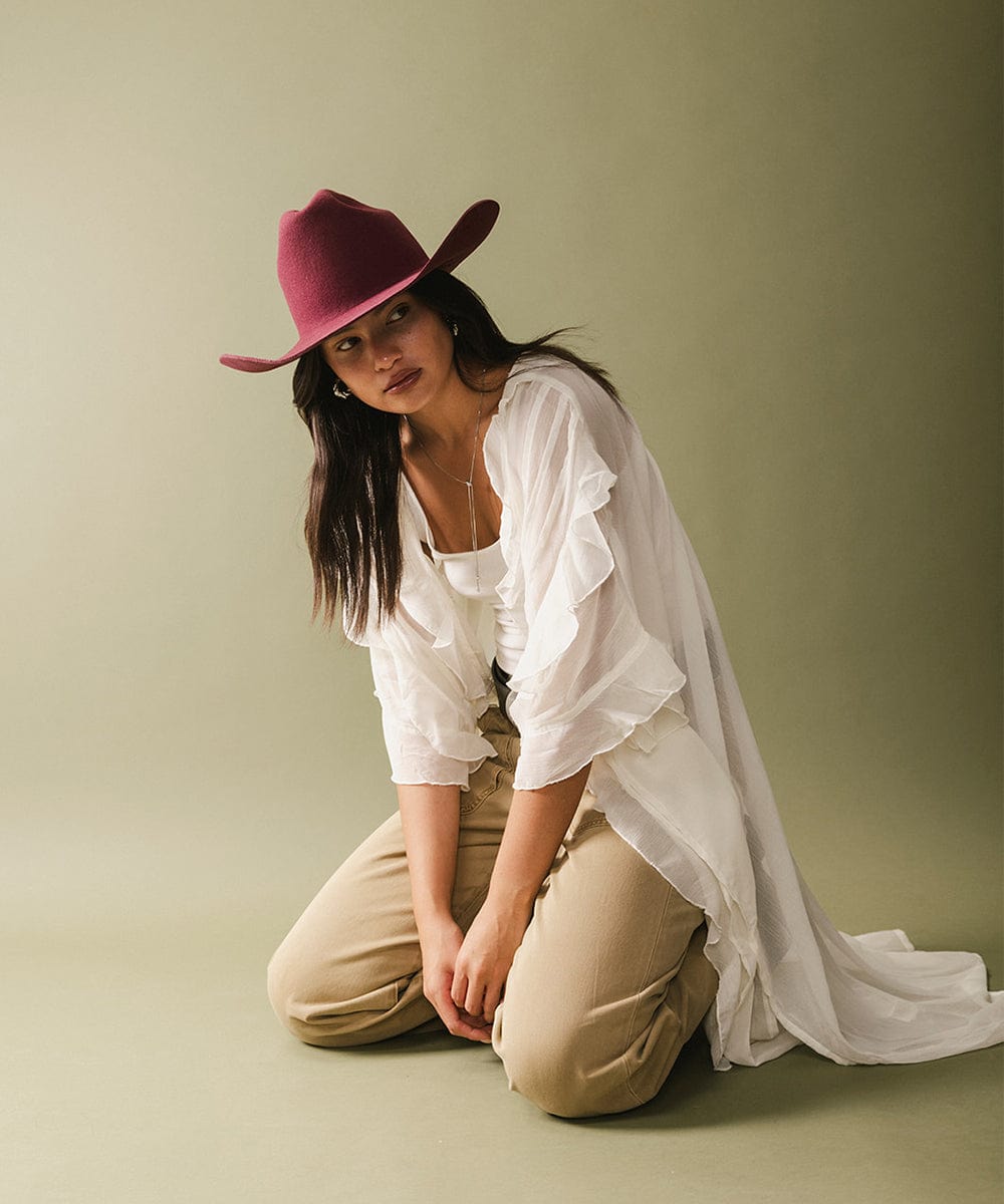 Woman wearing a white blouse and beige pants with a maroon hat on a plain background #color_merlot