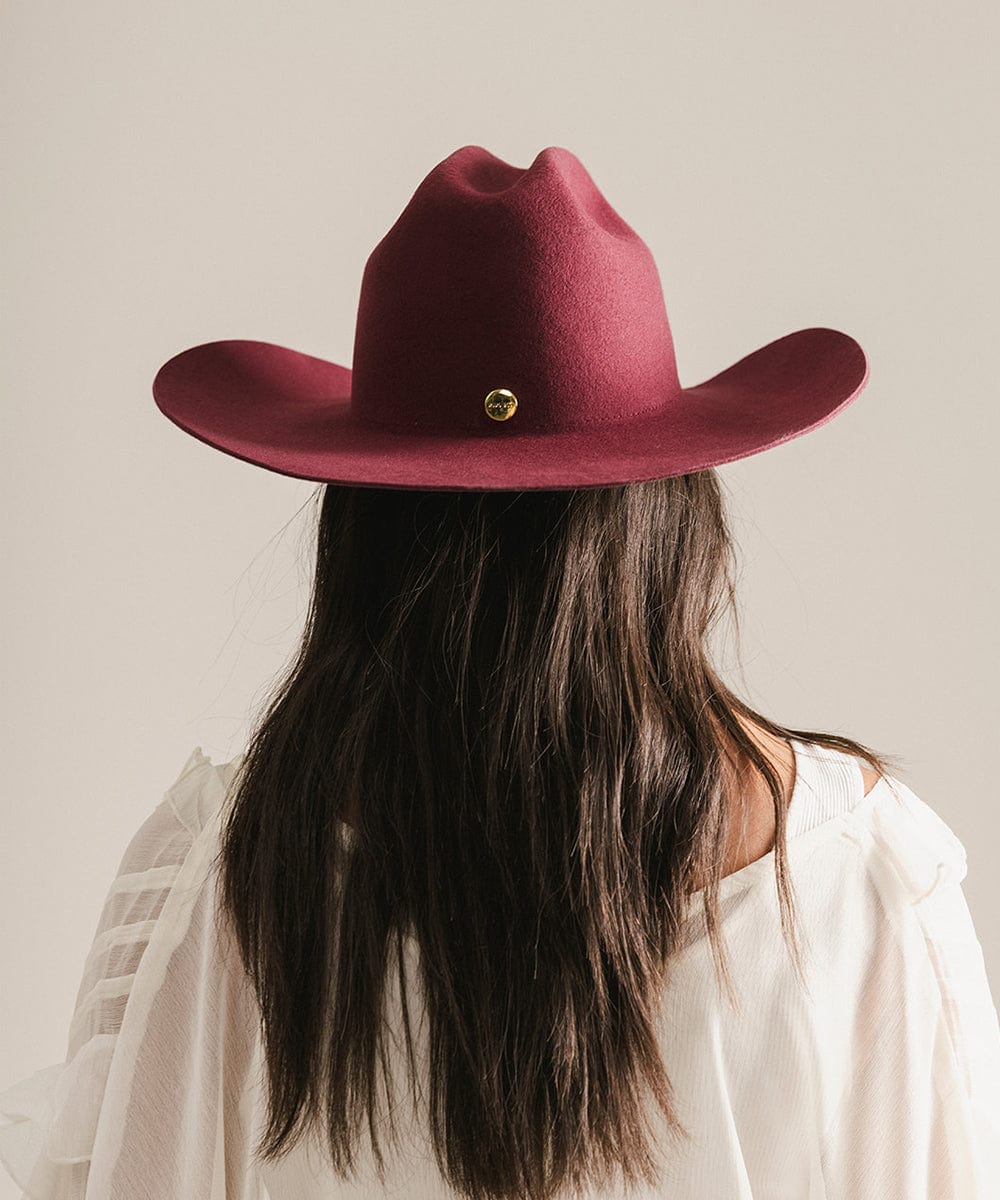 Person wearing a maroon cowboy hat with a gold button on a neutral background #color_merlot