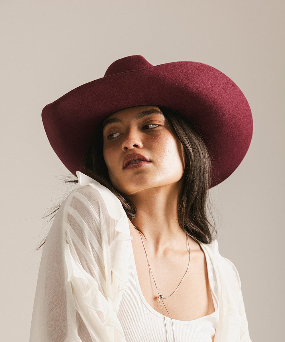 Woman wearing a wide-brimmed maroon hat against a plain background #color_merlot