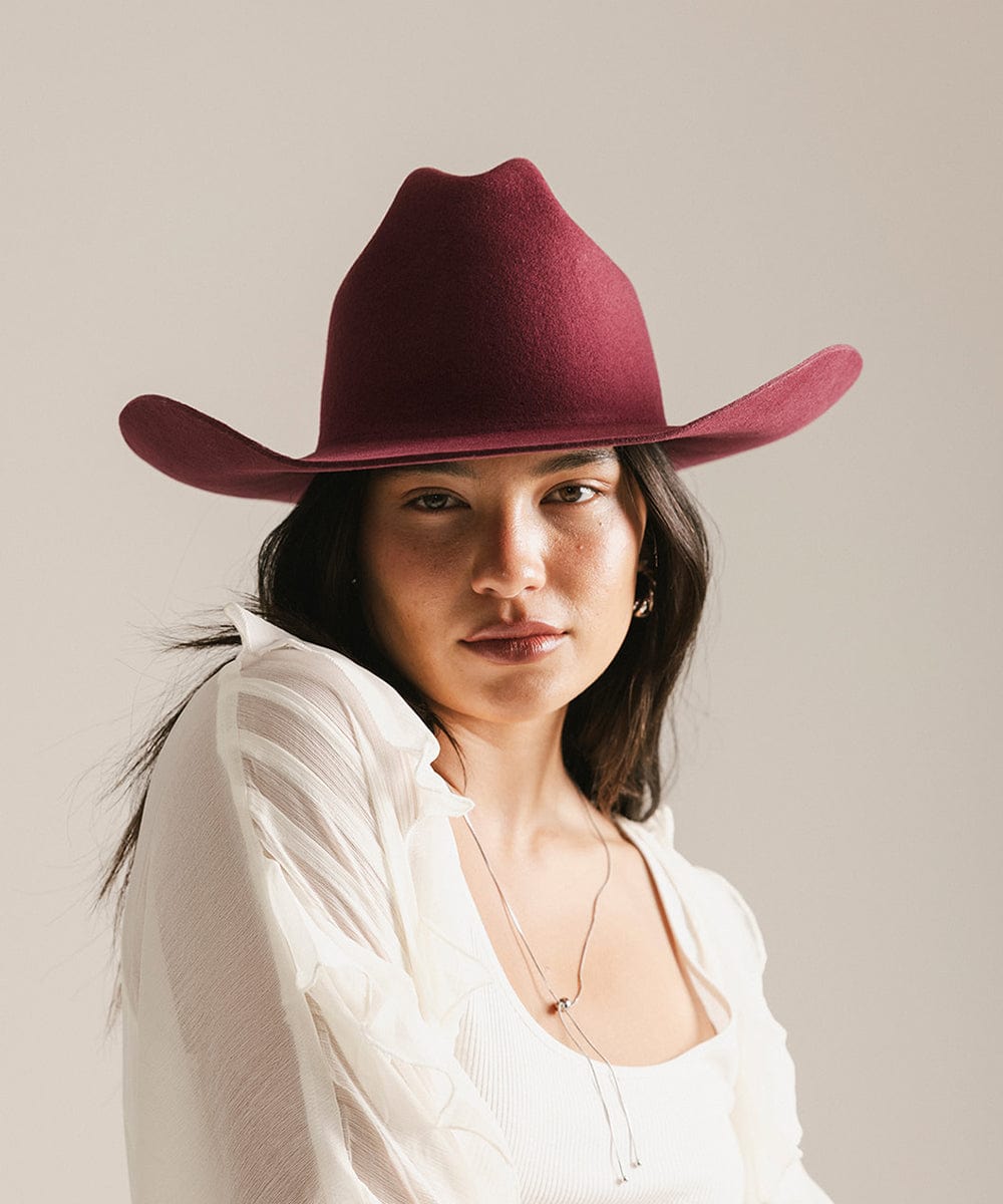 Woman wearing a maroon cowboy hat against a plain background #color_merlot
