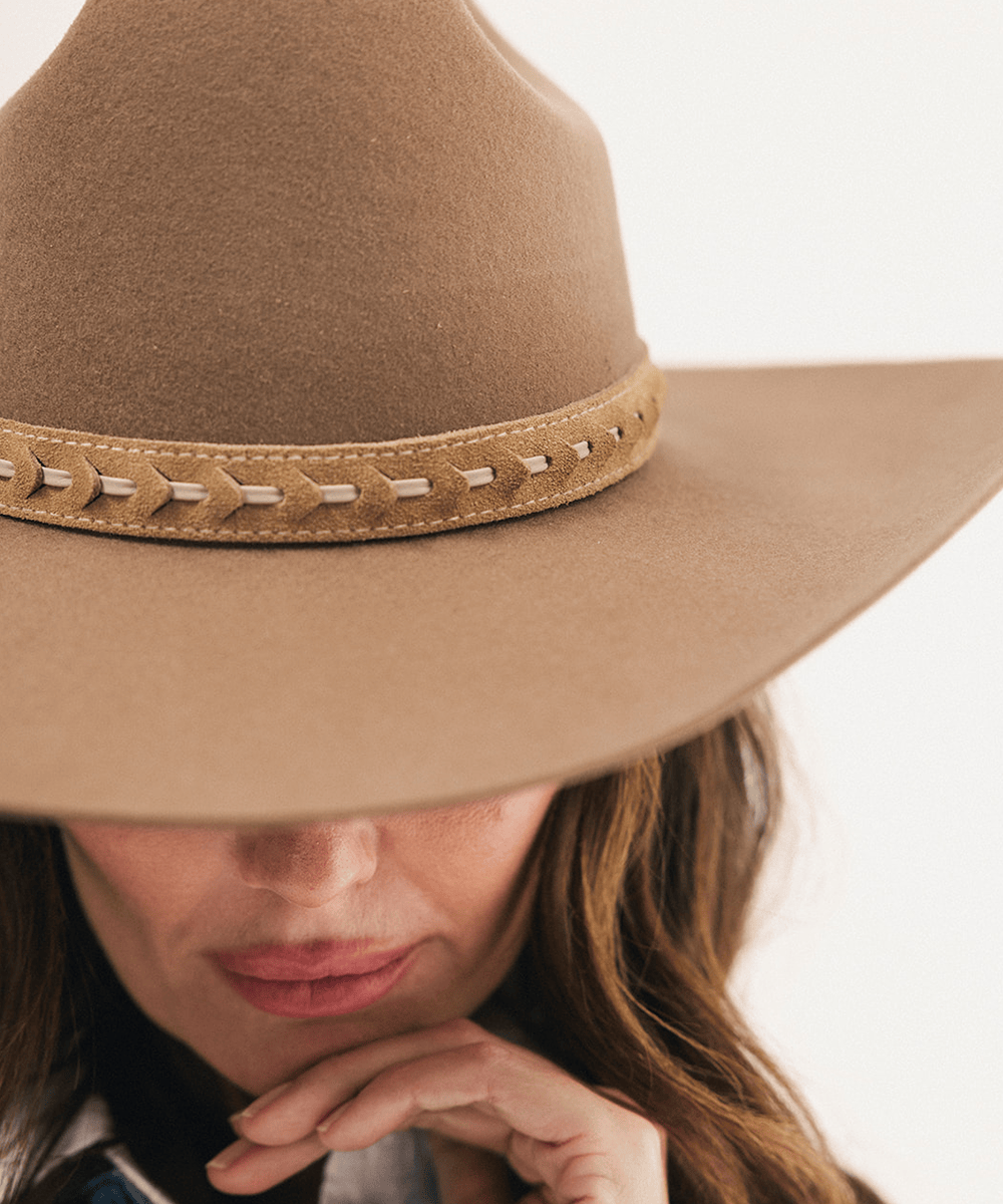 Close-up of a woman wearing a tan wide-brim felt cowboy hat with a stitched leather band, against a plain white background #color_camel