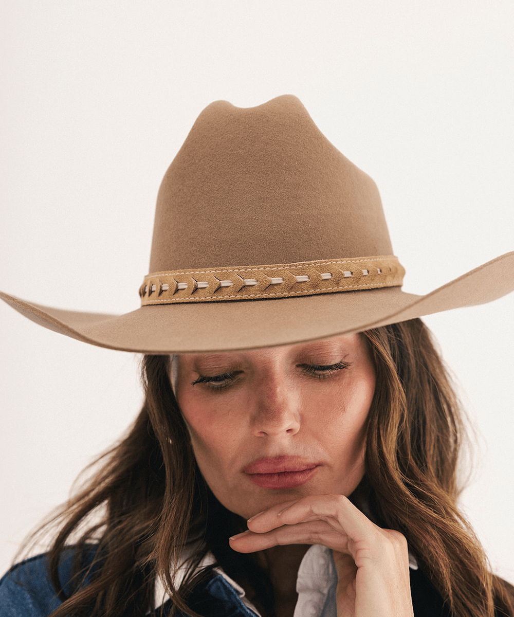 A woman wearing a tan cowboy hat with a decorative band of metallic studs, shown in a close-up portrait against a plain light background #color_camel