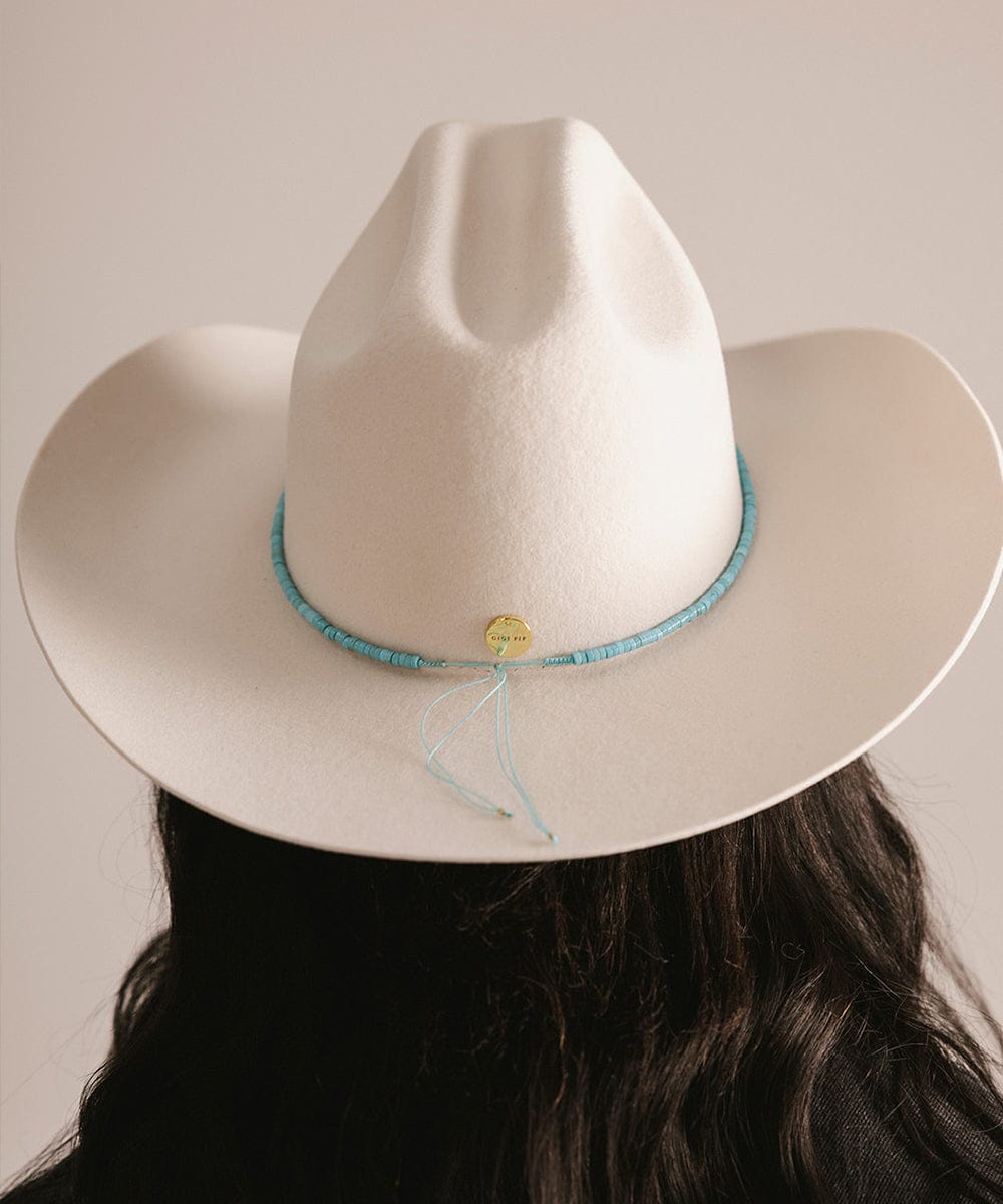 White cowboy hat with a blue band worn by a person against a neutral background #color_turquoise