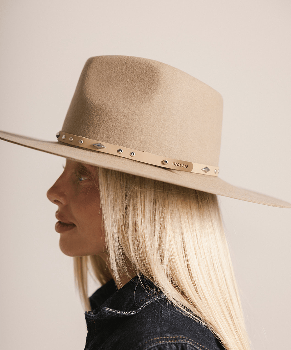 Woman wearing a cream hat with a tan studded leather hat band against a plain background #color_tan