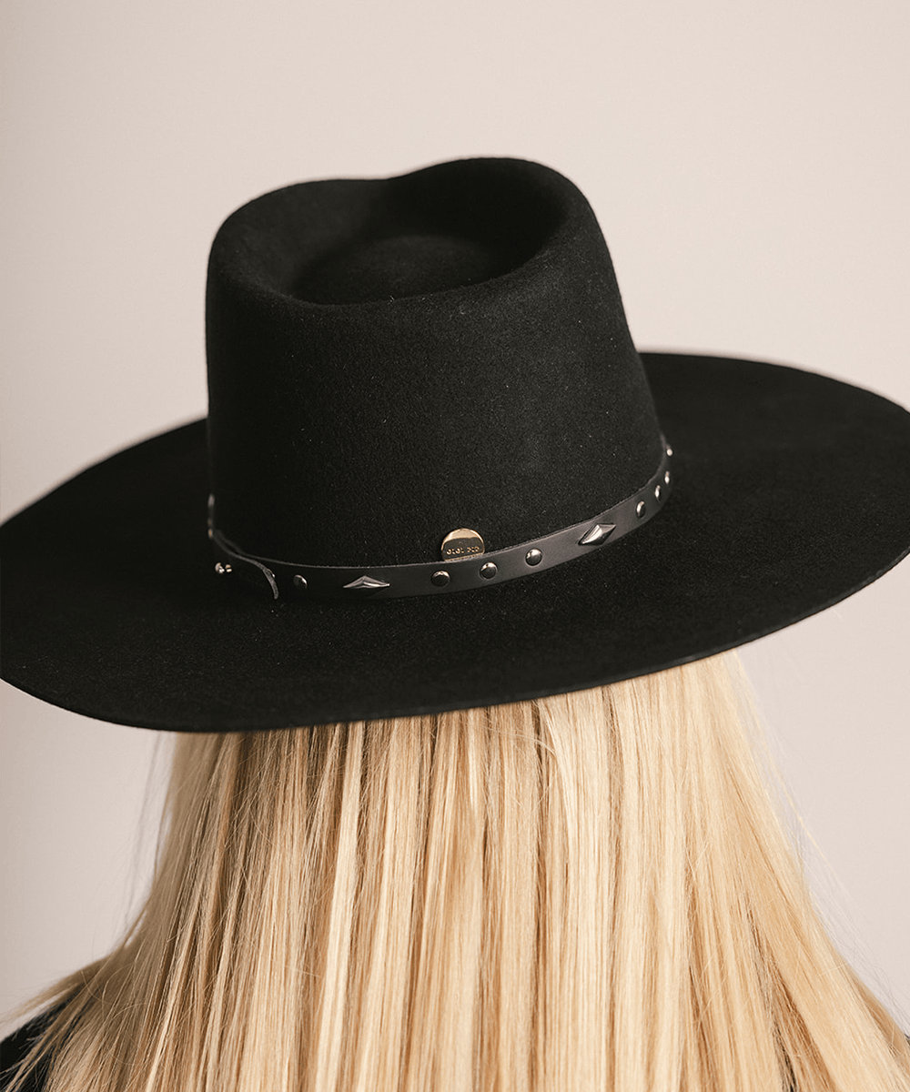 Woman wearing a black hat with a black studded leather hat band against a plain background #color_black