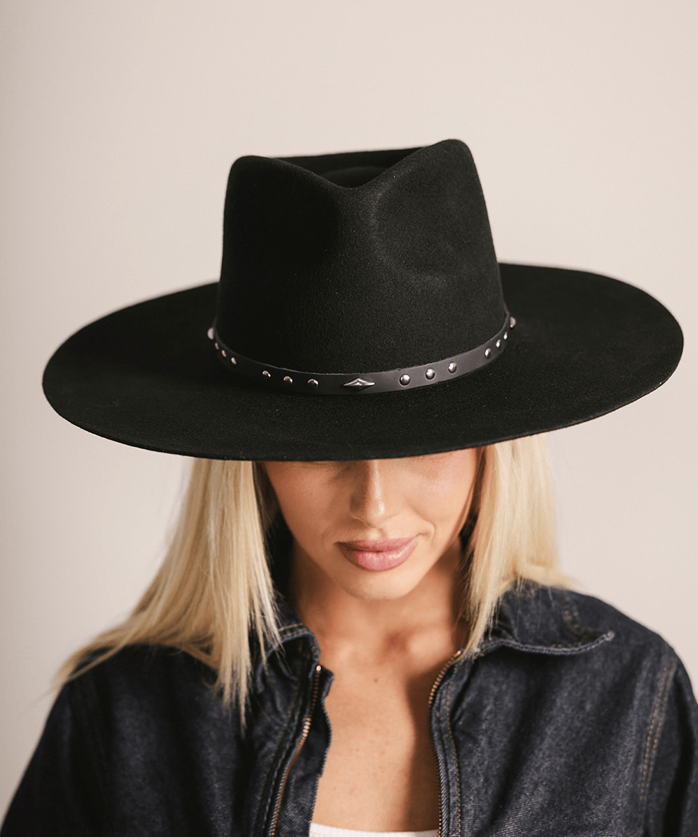 Woman wearing a black hat with a black studded leather hat band against a plain background #color_black