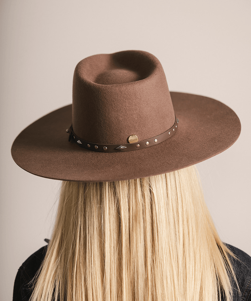 Woman wearing a brown hat with a chocolate colored studded leather hat band against a plain background #color_chocolate