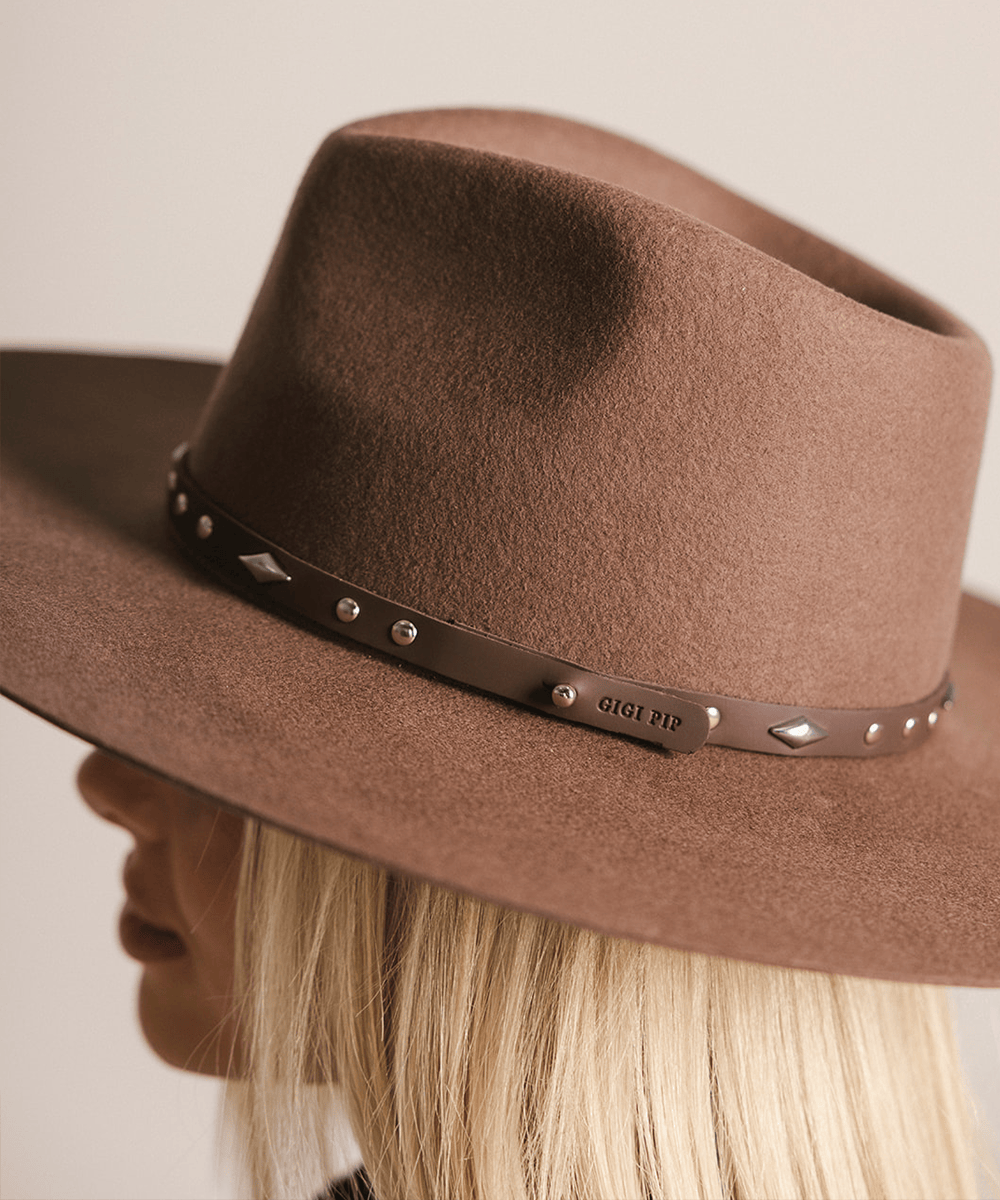 Woman wearing a brown hat with a chocolate colored studded leather hat band against a plain background #color_chocolate