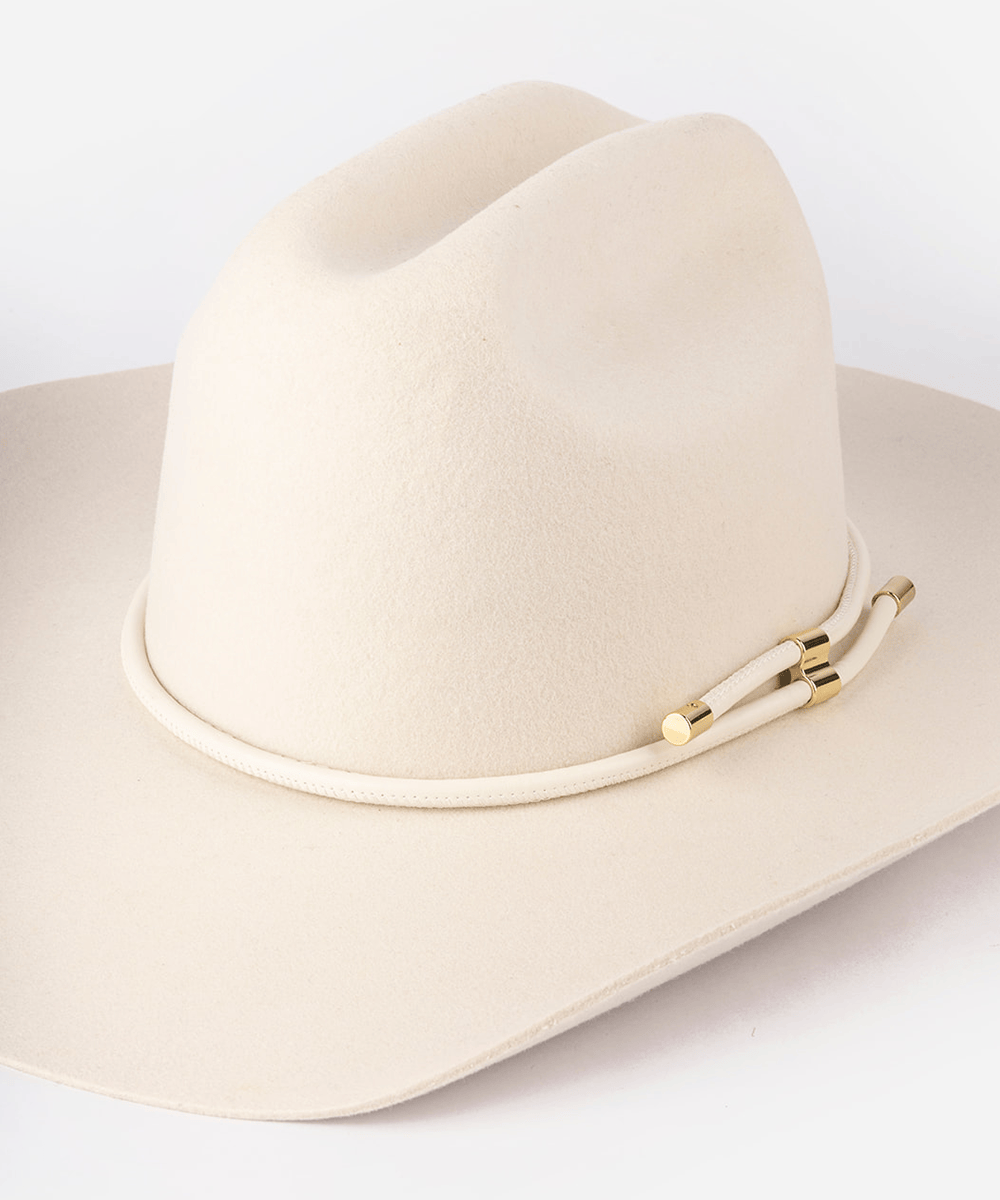A cream-colored felt cowboy hat with a matching rope band and gold-toned metal accents, photographed on a clean white background #color_off white