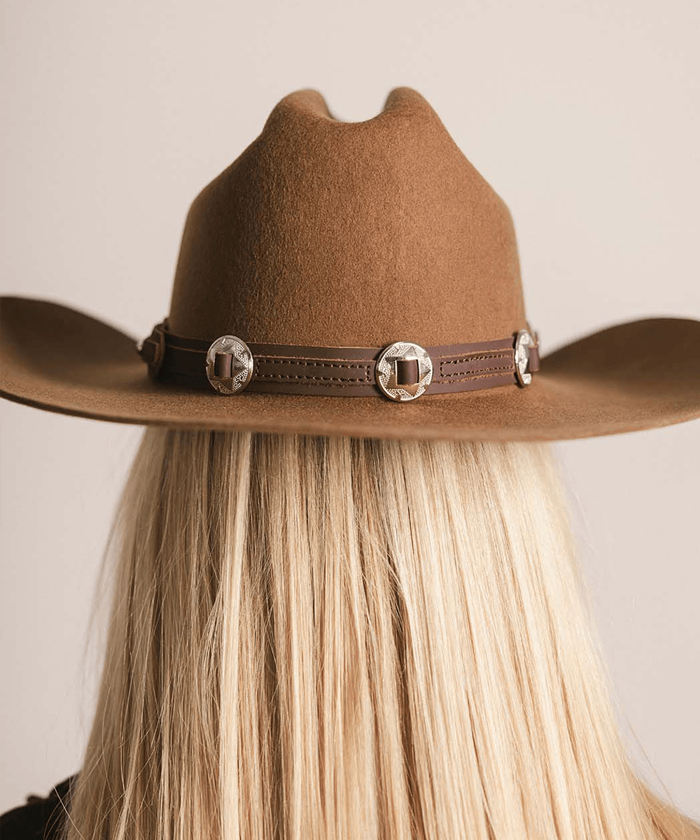 Brown cowboy hat with decorative band worn by a person with blonde hair, on a neutral background #color_chocolate