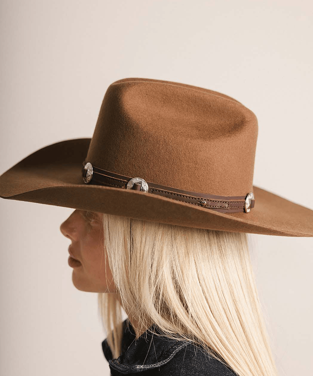 Brown cowboy hat with decorative band worn by a person with blonde hair on a neutral background #color_chocolate