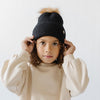 Gigi Pip beanies for kids - Milo Beanie - soft knit ribbers kid's beanie featuring a fold up brim with a rose gold Gigi Pip logo pin on the side of the fold and a pom pom on the center of the crown [midnight]