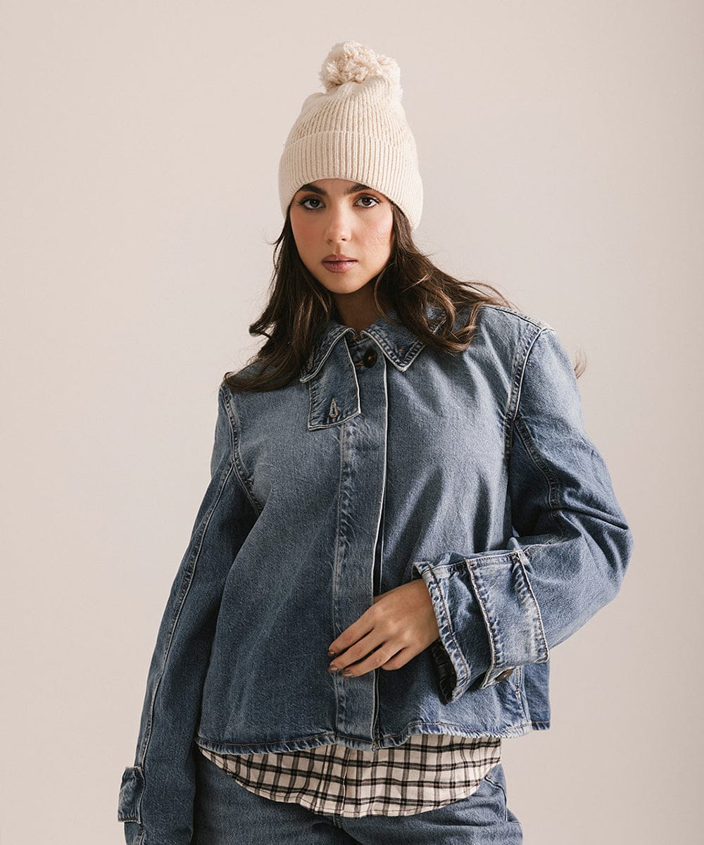 Woman wearing a denim jacket, checkered shirt, and white beanie against a plain background #color_cream