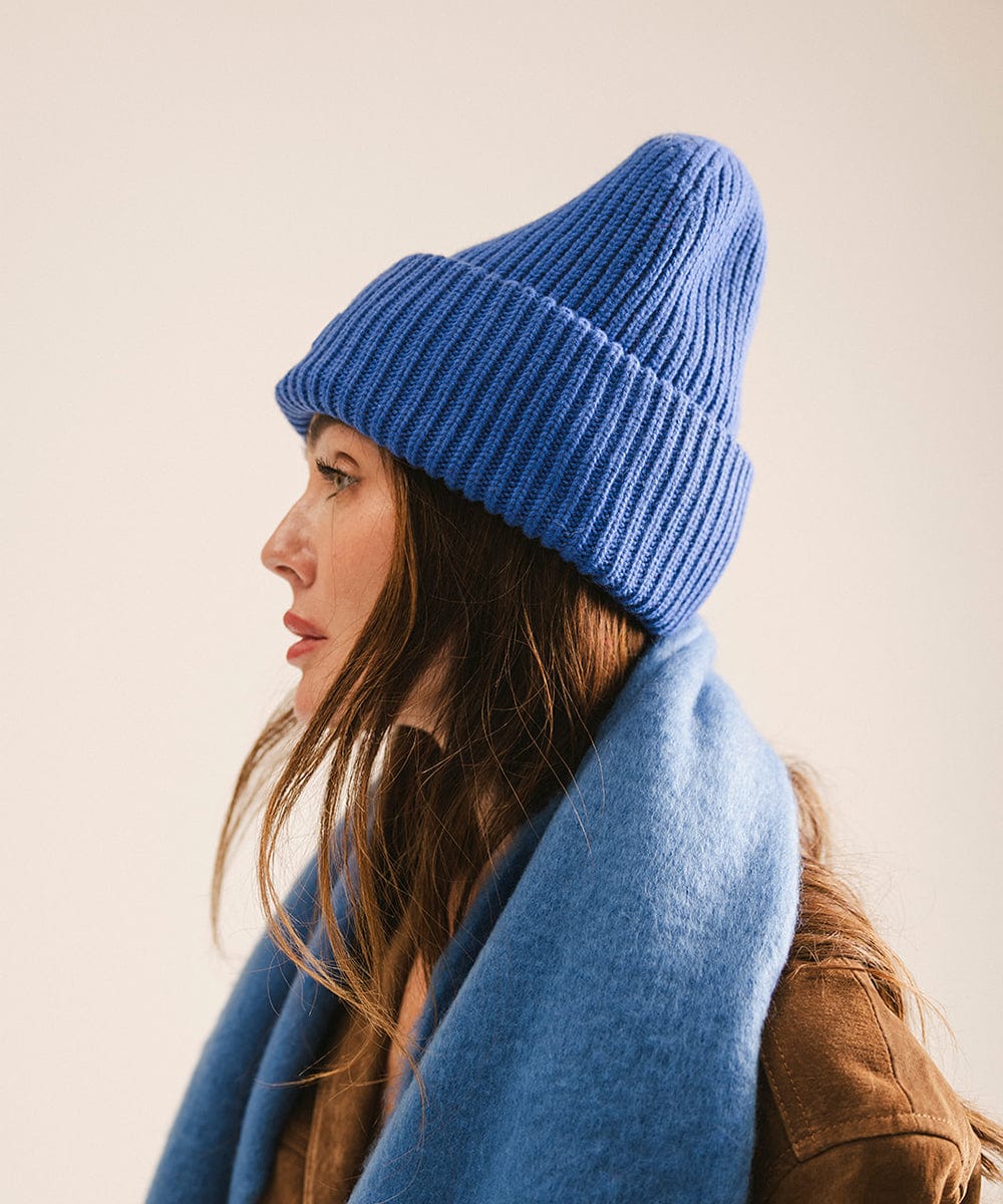 Woman wearing an alpine blue knit beanie and scarf, facing sideways against a plain background #color_alpine blue
