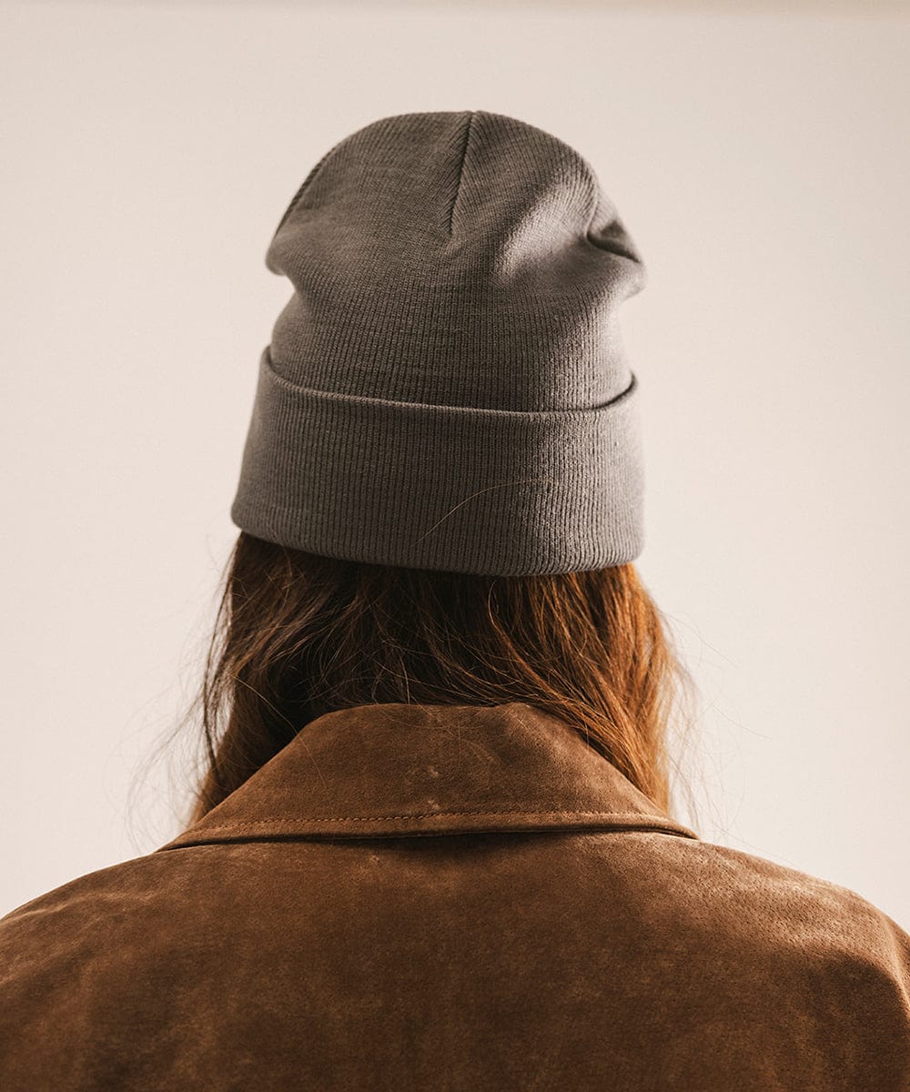 Person wearing a grey beanie and brown coat, facing behind against a neutral background #color_grey
