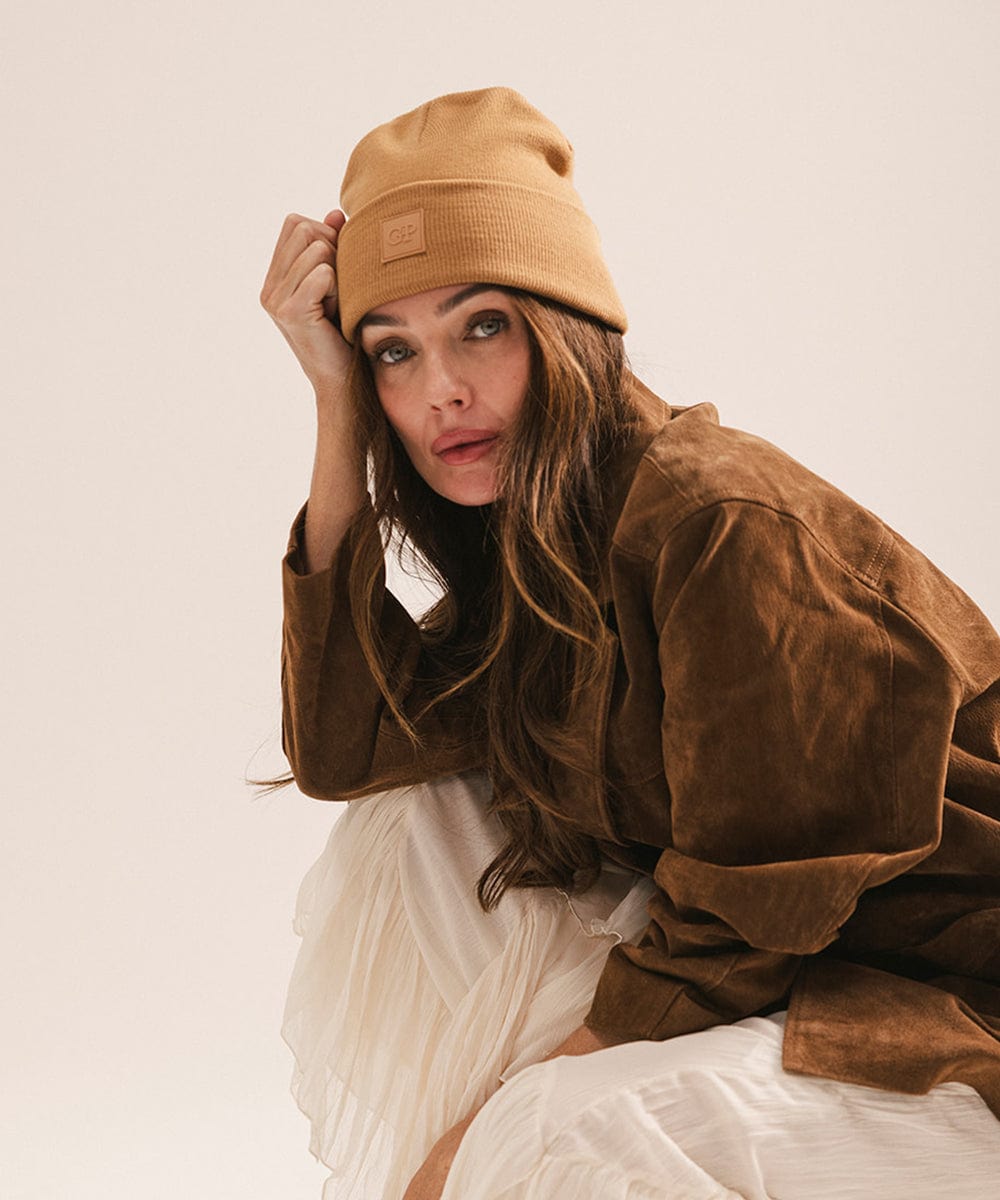 Woman wearing a latte colored beanie and jacket against a plain background #color_latte