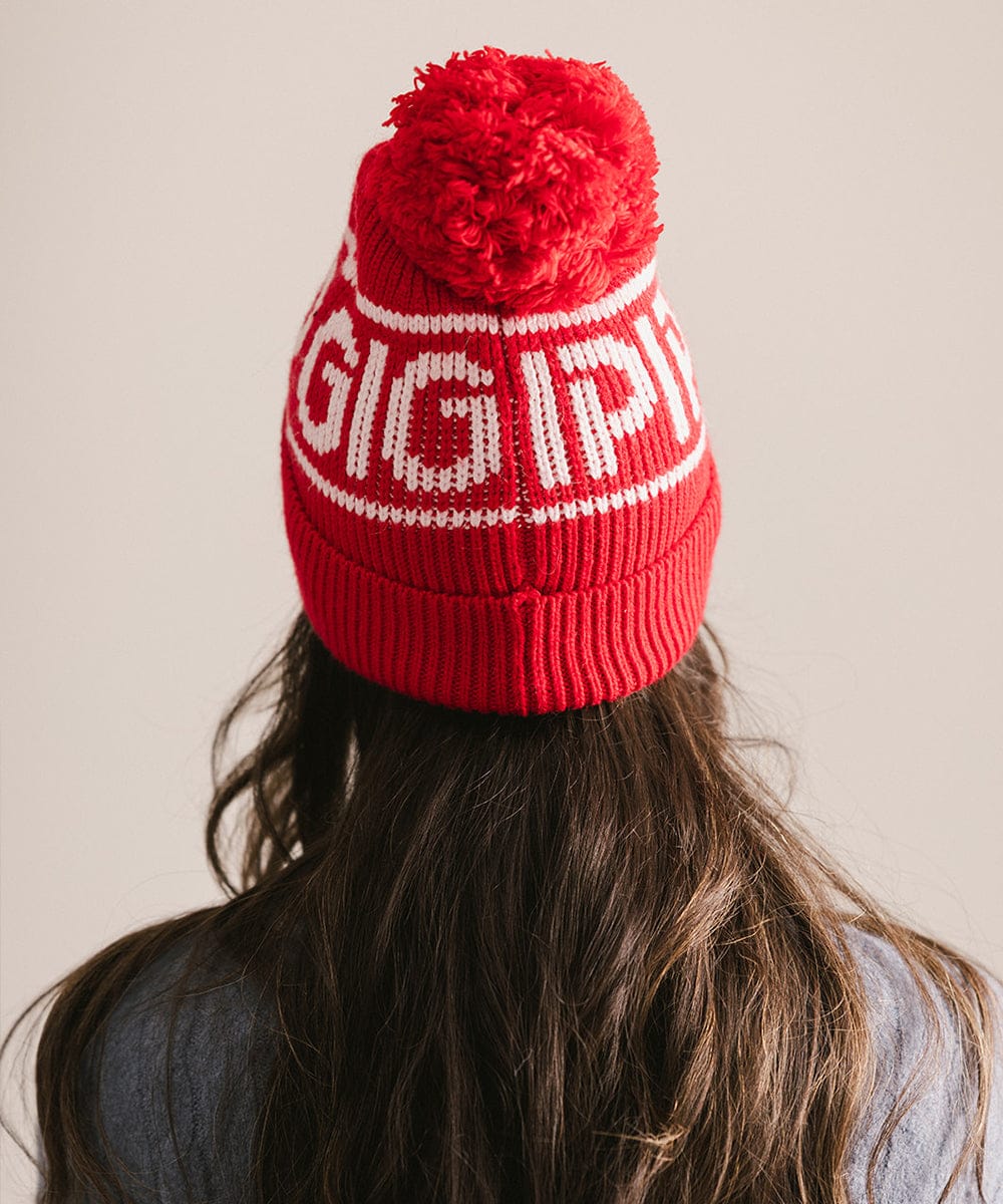 Red knit beanie with white text worn by a person against a neutral background #color_ruby red