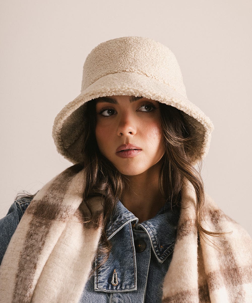 Woman wearing a cream sherpa bucket hat and a black coat against a plain background #color_cream