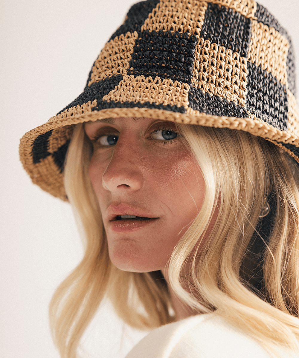 Woman wearing a black checkered crochet packable bucket hat made from paper straw, displayed against a white background. #color_black check