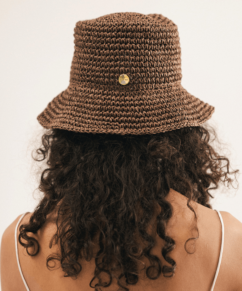 Woman wearing a brown woven bucket hat against a plain background #color_chocolate