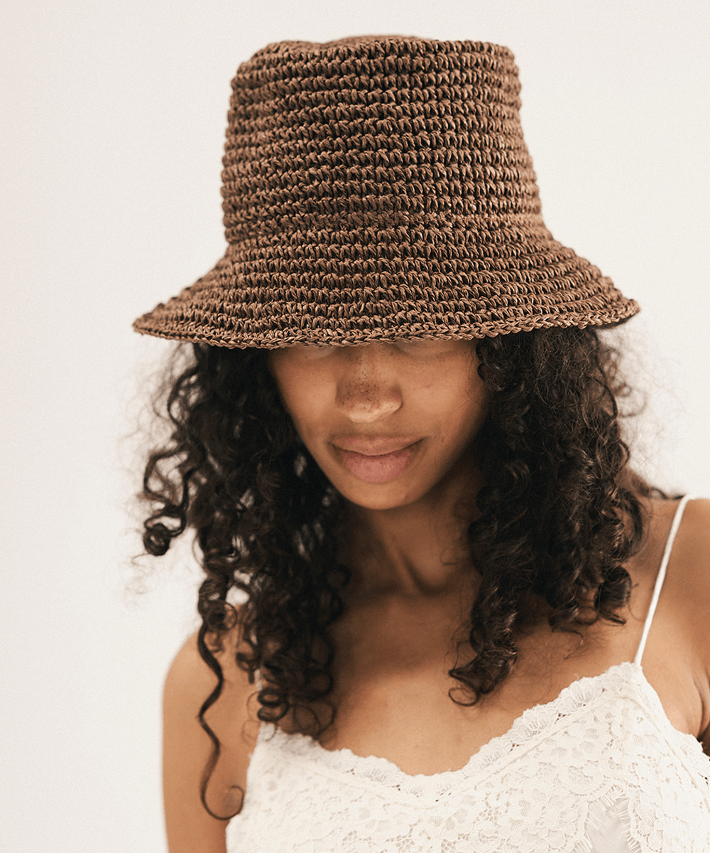 Woman wearing a brown woven bucket hat against a plain background #color_chocolate