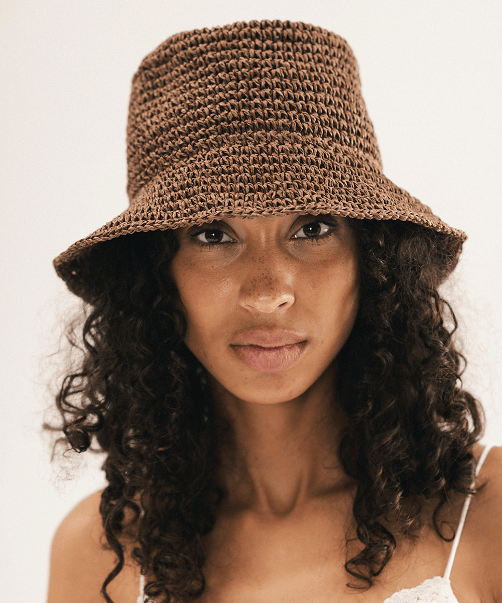 Woman wearing a brown woven bucket hat against a plain background #color_chocolate