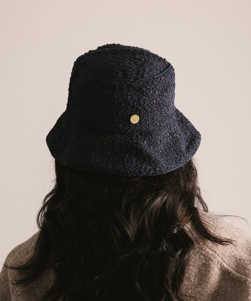 Person wearing a navy textured bucket hat with a gold button on a beige background #color_navy