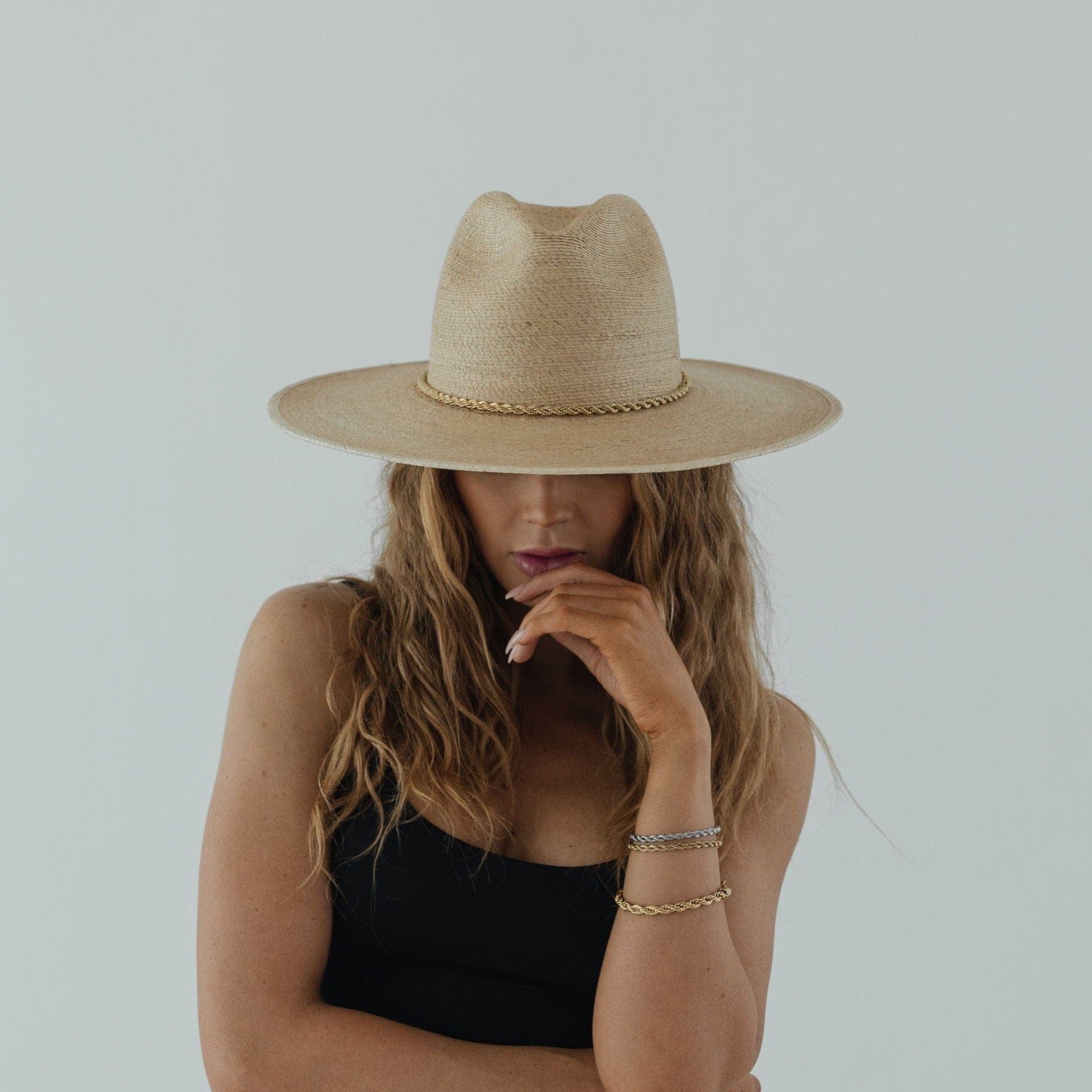 Woman wearing a toasted colored straw hat with a gold chain and a black top against a plain background #color_toasted