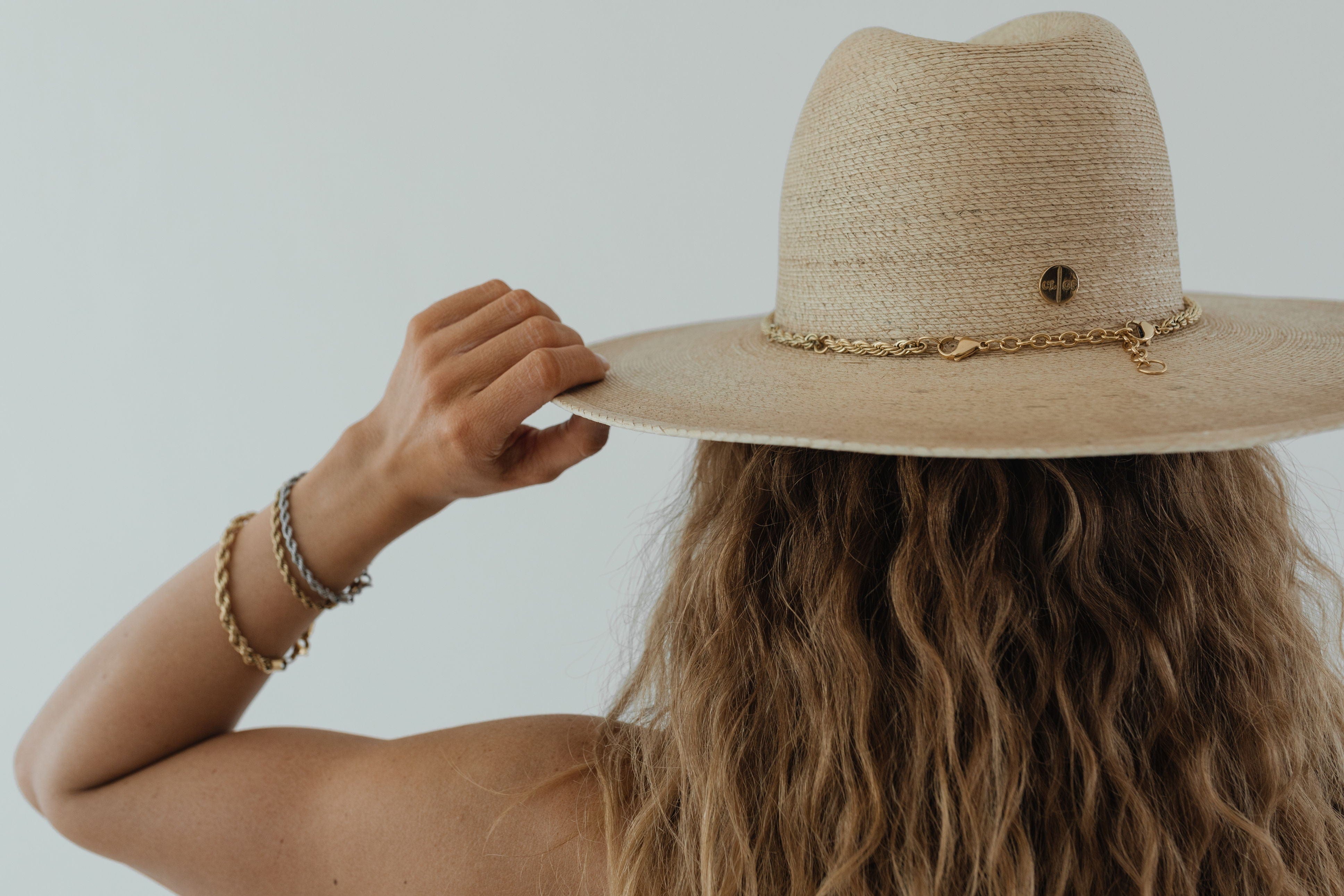 Woman wearing a toasted colored straw hat with a gold chain facing behind against a plain background #color_toasted