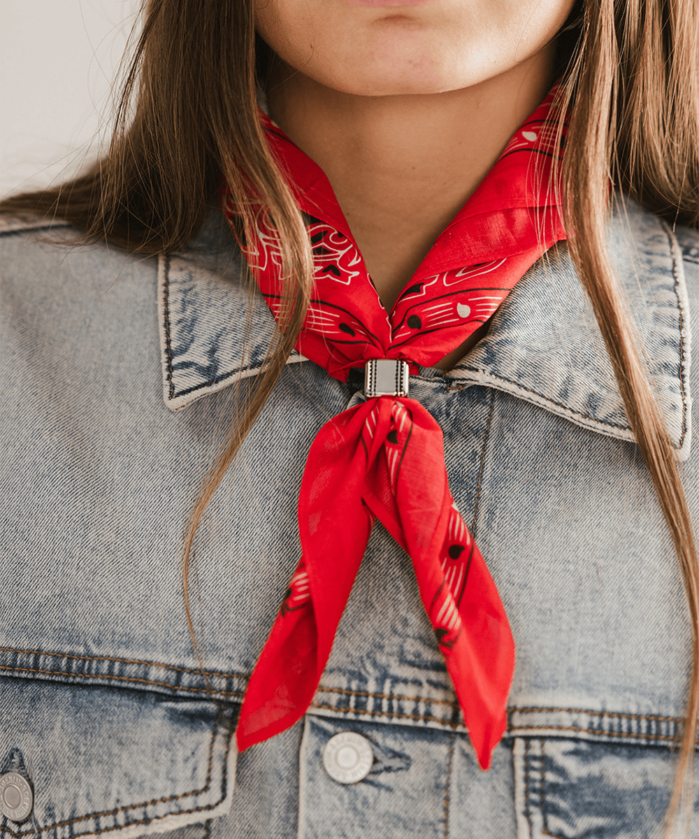 Person wearing a red bandana and Aztec Square Concho Bandana Slide tied around their neck with a denim jacket. #color_silver