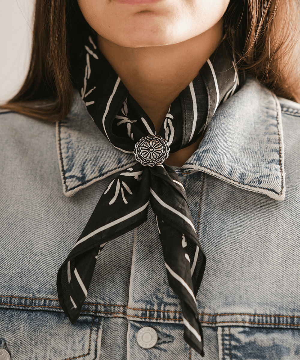 Person wearing a black and white patterned scarf tied with a Sunburst Concho Bandana Slide and wearing a denim jacket #color_silver