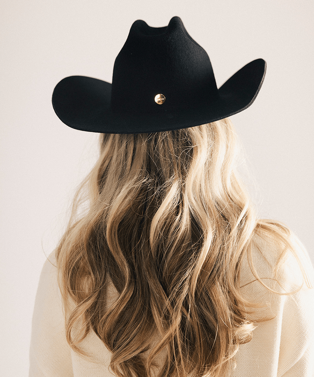 Woman wearing a black cowboy hat and cream sweater against a plain background #color_black