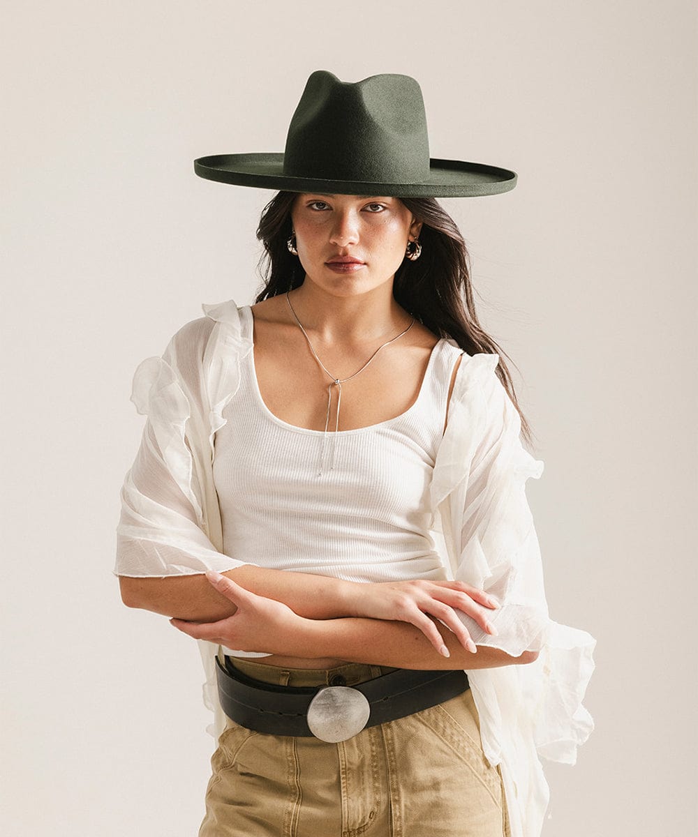 Woman wearing a wide-brimmed black hat and white blouse against a plain background #color_dark green
